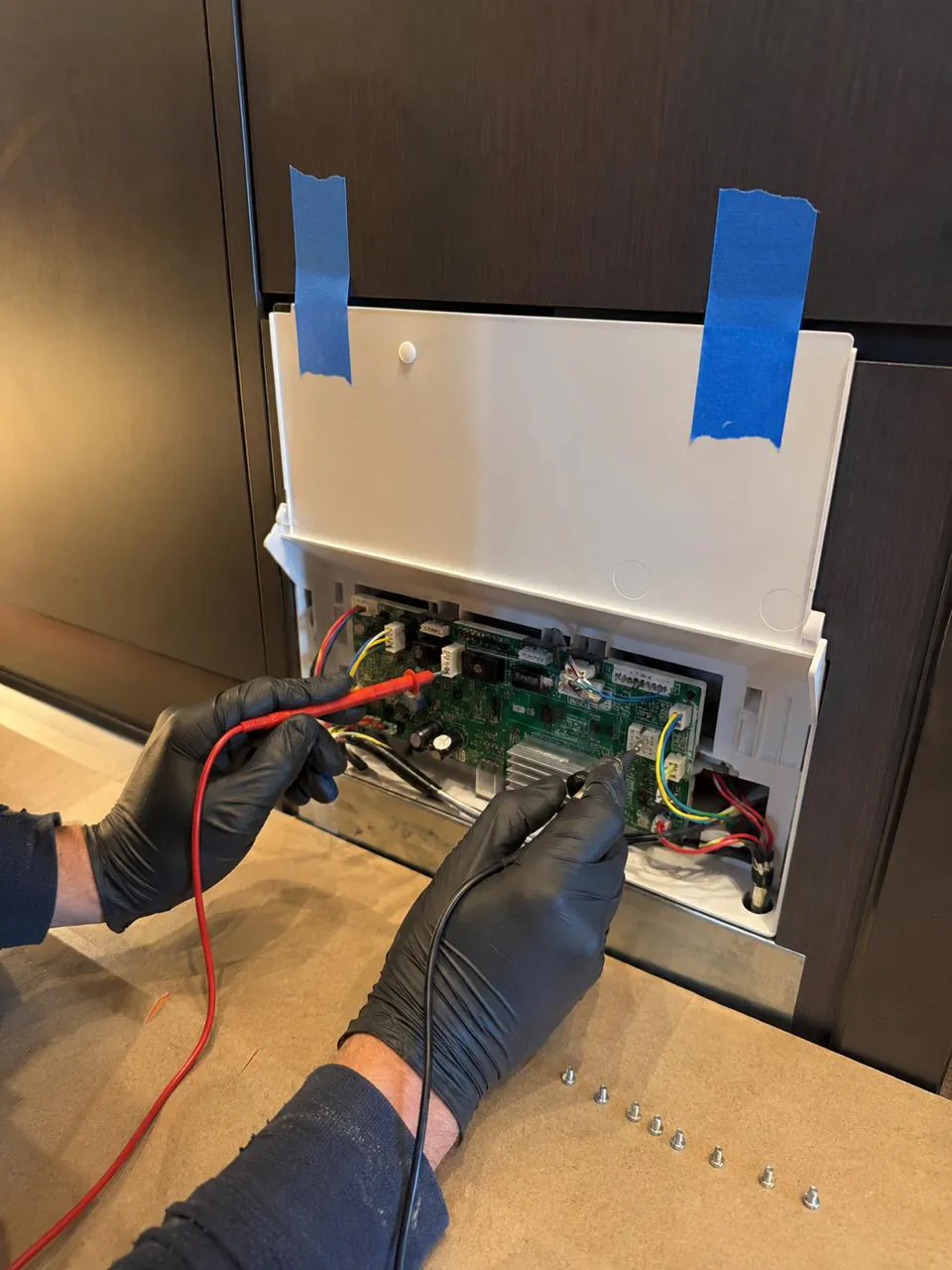 Technician testing dishwasher control board with multimeter during repair