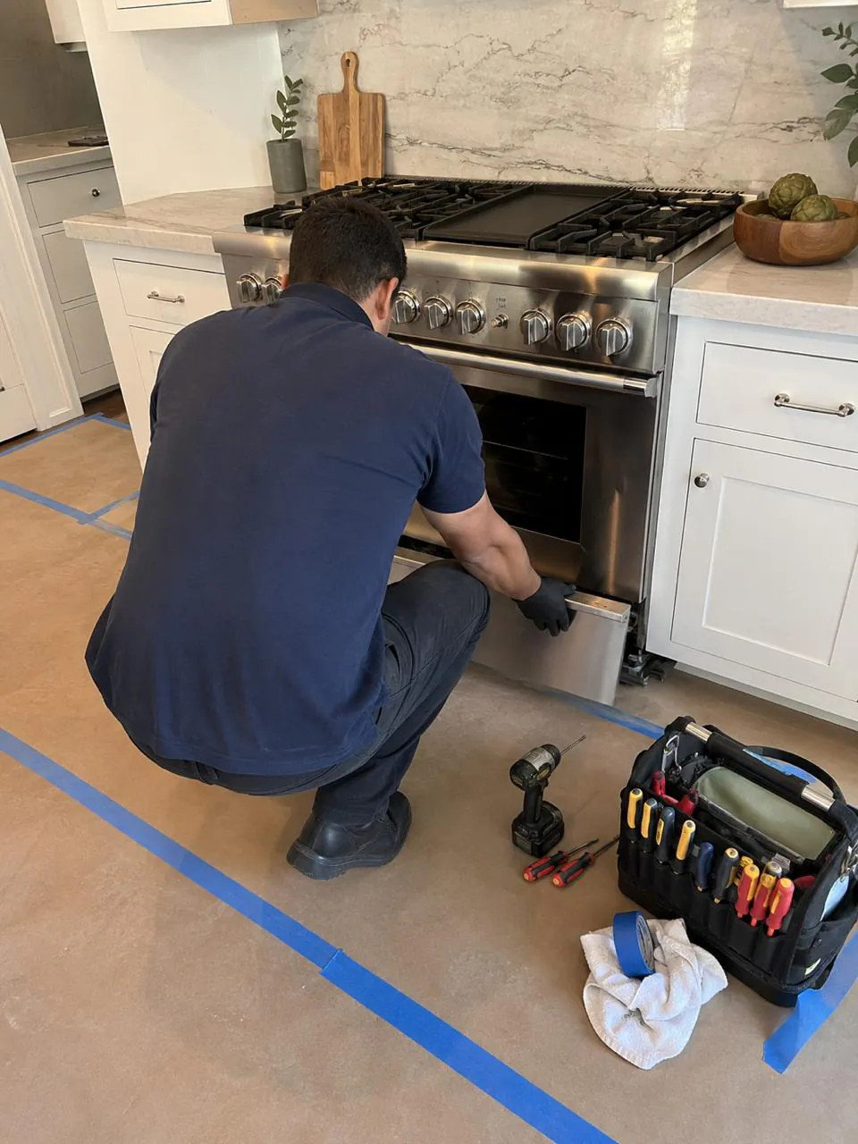 Technician repairing stainless gas range oven in San Diego kitchen