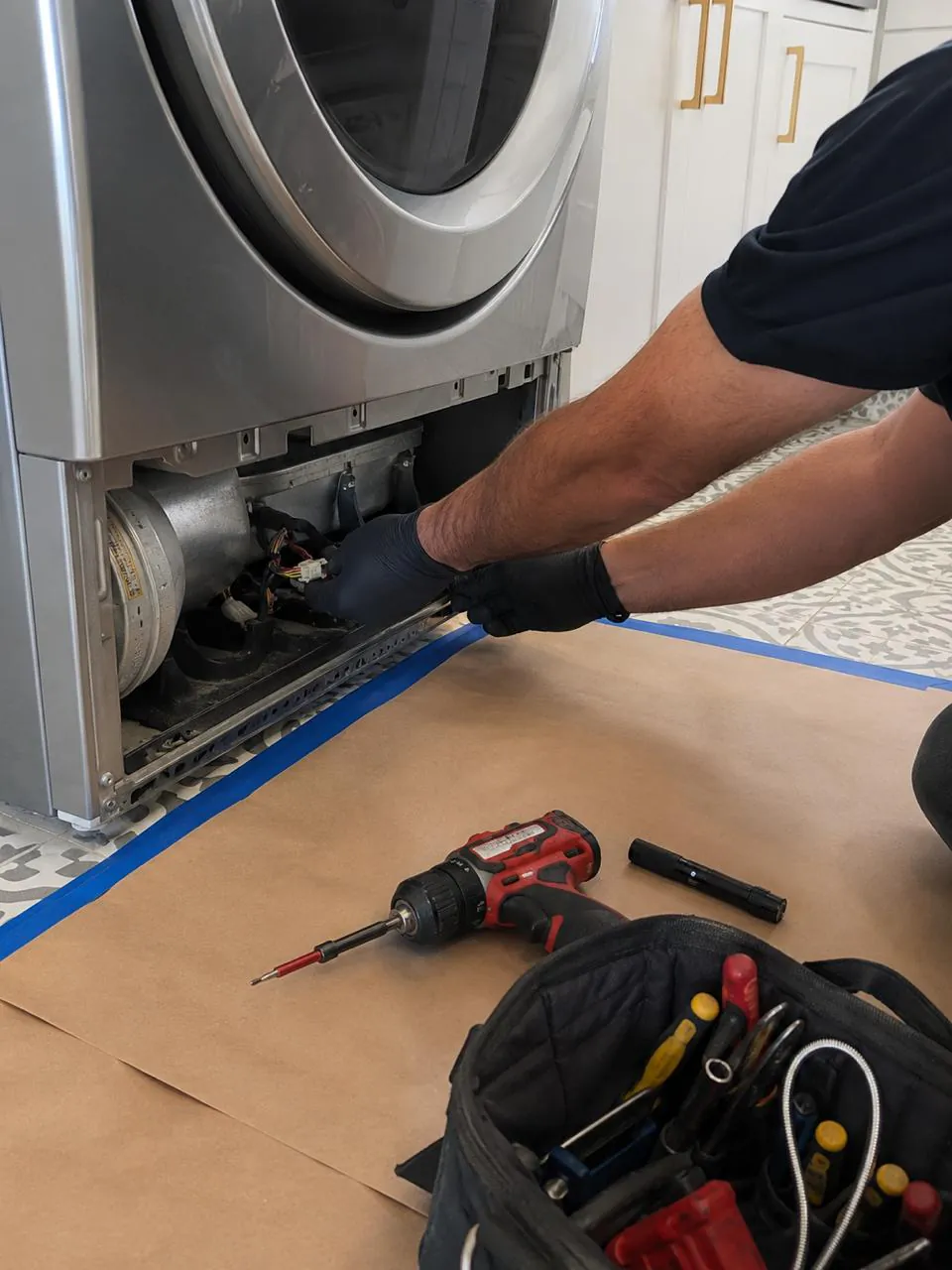 Technician repairing front-load dryer wiring with drill and tools